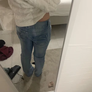 Ljusblå raka jeans med låg midja - Säljer ett par ljusblå jeans med låg midja och raka ben. Jeansen har klassiska fickor både fram och bak samt snygga slitningar för en avslappnad look. Perfekta för dig som gillar en chill och enkel stil.