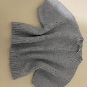 Ljusblå stickad tröja med kort ärm - Supermysig ljusblå stickad tröja med korta ärmar och rund hals. Tröjan har breda ribbade muddar vid ärmslut och nederkant, vilket ger en chill och modern vibe. Perfekt för lager-på-lager och att styla med jeans eller kjol.