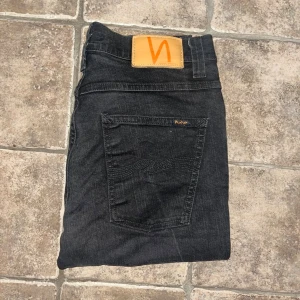 Nudie Jeans - Svarta jeans från Nudie Jeans slim Jim. Jeansen har rak passform och är tillverkade i bomull med en stilren look. Perfekta för dig som gillar en enkel men stilren vibe. Midja 37cm, längd 105cm. JAG SKICKAR EJ FLER BILDER NÄR JAG BÄR JEANSEN! för storleksguide hänvisar jag till måtten och för bättre inblick i passformen rekommenderar jag att googla på modellnamnet. Jeansen kan vara uppsydda utan att jag noterat det så kolla måtten noggrant :) s4