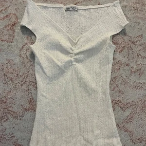 Vit topp zara - Supersöt vit topp från Zara med smockat material. Toppen har v-ringning, korta ärmar och en snygg rynkdetalj framtill. Perfekt att styla med jeans eller kjol för en fräsch look.