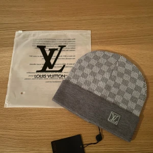 Grå rutig mössa - Snygg grå mössa med rutigt mönster och bred uppvikt kant. Loggan framtill ger en exklusiv vibe. Perfekt för dig som vill ha en stilren och lyxig accessoar till vintern.