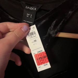 Svart sammetstopp med asymmetrisk hals - Säljer en svart långärmad topp från Lindex i mjuk sammet med en cool asymmetrisk halsringning. Toppen har en tight passform och ger en lyxig känsla med sitt glansiga material. Perfekt för dig som vill sticka ut med en unik detalj i din outfit.