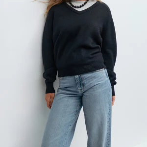 Mörkblå v-ringad stickad tröja  - Svart stickad tröja från Gina Tricot med v-ringad hals och långa ärmar. Tröjan har ribbade muddar vid ärmslut och nederkant, vilket ger en snygg och enkel look. Perfekt att matcha med jeans eller kjol för en chill stil. Endast använd två gånger.