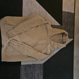 Beige hoodie med huva och snörning - Säljer en stilren beige hoodie med huva och snörning. Tröjan har långa ärmar och ribbade muddar vid ärmslut och nederkant. Perfekt för en chill och avslappnad look. 