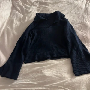 Mörkblå stickad tröja från Gina Tricot - Mysig mörkblå stickad tröja från Gina Tricot med krage och v-ringning. Tröjan har långa ärmar och breda ribbade muddar vid ärmslut och nederkant. 