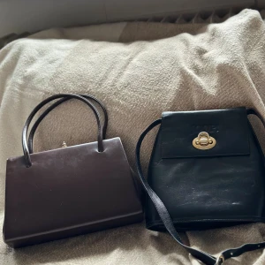 Svart axelväska från JOOP! och brun handväska - Säljer en svart axelväska från JOOP! i skinn med guldfärgad låsdetalj och randigt innerfoder, samt en stilren brun handväska i skinn med klassisk form och guldfärgad knäppning. Perfekt för dig som gillar tidlös design och snygga detaljer.