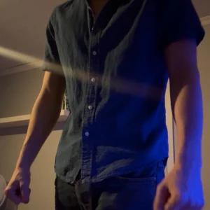 Blå kortärmad skjorta från Polo Ralph Lauren - Snygg blå skjorta från Polo Ralph Lauren med korta ärmar och klassisk krage. Skjortan har knappar framtill och den ikoniska broderade loggan på bröstet. Tillverkad i mjuk bomull som känns skön mot huden. Perfekt för dig som gillar stilren och enkel design.