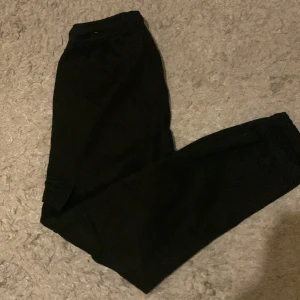 Svarta cargobyxor från Zara - Svarta cargobyxor från Zara med elastisk midja och muddar vid benslut. Byxorna har klassiska cargofickor på sidorna och är tillverkade i ett mjukt bomullsmaterial. Perfekta för en avslappnad och trendig look.