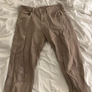 Beige byxor från Vailent i bomull (Carlings) - Snygga beige byxor från Vailent i storlek M, tillverkade i 100% bomull. Modellen har klassisk femficksdesign, bälteshällor och raka ben. Perfekt för dig som gillar en enkel och clean stil. Färgen är neutral och passar till det mesta.