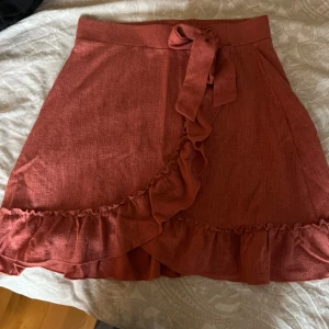 Kjol  - Supersöt koralfärgad kortkjol från Gina Tricot i omlottmodell med knytband i midjan och volangdetaljer längs kanterna