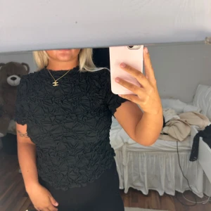 Svart strukturerad topp från Vero Moda - Säljer en svart kortärmad topp från Vero Moda med unik strukturerad och rynkad yta. Toppen har rund halsringning och sitter figurnära. Perfekt för dig som vill ha något annorlunda och trendigt i garderoben.