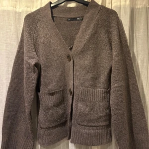 Brun stickad kofta från 157 XS - Mysig brun stickad kofta från 157 i storlek XS. Koftan har v-ringning, två stora fickor fram och stängs med knappar. Ribbstickade muddar vid ärmslut och nederkant ger en chill vibe. Perfekt att slänga på över en t-shirt eller linne.