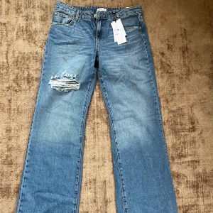 Wide jeans med slitning från Gina Tricot - Blåa wide leg jeans från Gina Tricot i modellen 'tall', med låg midja och breda ben. Jeansen har en snygg slitning på ena låret och klassisk femficksdesign. Perfekta för dig som gillar en avslappnad och trendig look.