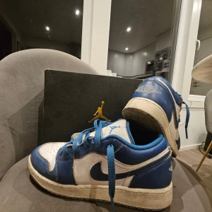Nike Air Jordan 1 Low blå/vit 38.5 - Säljer ett par Nike Air Jordan 1 Low i blått och vitt med klassisk Jumpman-logga på plösen. Skorna har blå snörning, perforerad tåbox och vit sula. Tillverkade i skinn och syntetmaterial, perfekt för dig som gillar streetwear och sneakers med retrovibe.