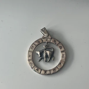 Silverfärgat halsband med zodiak och oxe - Unikt halsband i silverfärg med en rund berlock prydd av zodiaksymboler och en detaljrik oxe i mitten. Perfekt för dig som gillar astrologi och vill ha ett personligt smycke med cool vintagekänsla. S925 äkta silver 
