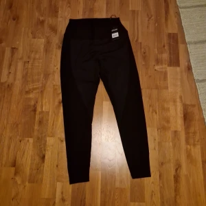 Svarta leggings från Carlheim, M - Svarta leggings från Carlheim i storlek M, tillverkade av 88% nylon och 12% spandex. De har en ribbad struktur och hög midja som ger en snygg och bekväm passform. Perfekta för träning eller chill dagar. Snyggt minimalistiskt märke på insidan.