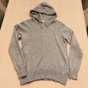 Grå cashmere hoodie från Sayless - Mjuk och lyxig grå hoodie från Sayless i 100% cashmere XXS. Tröjan har huva med snörning och långa ärmar, samt ribbade muddar vid ärmslut och nederkant.