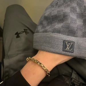 Grå blå Louis Vuitton mössa med rutmönster - Snygg grå blå  mössa från Louis Vuitton med diskret rutmönster och LV-logga framtill. Mössan har en bred uppvikt kant och är tillverkad i mjukt material som känns lyxigt. Perfekt accessoar för att lyfta din outfit med exklusiv känsla.
