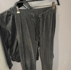 Mörkgrå mjukisbyxor i velour - Mysiga mörkgrå mjukisbyxor i sammetsmaterial med snörning i midjan. Byxorna har en avslappnad passform och är perfekta för chill dagar. Snyggt och stilrent plagg som är lätt att matcha med en hoodie eller t-shirt. Setet är i fint skick och ”färgskiftningarna” är inte så det är då det är velour material. Vid intresse skickas tydligare bilder där man ser att dem är i bra skick. Koftan är i XS och mjukisen i S