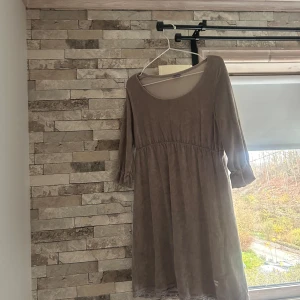 Grå klänning med broderad detalj - Säljer en grå klänning från me&i i storlek L. Klänningen har trekvartsärmar med lätt puff och rundad halsringning. Nedtill finns en broderad trollslända och spetskant. Materialet är mjukt och känns som bomull. Perfekt för dig som gillar enkla men fina detaljer.