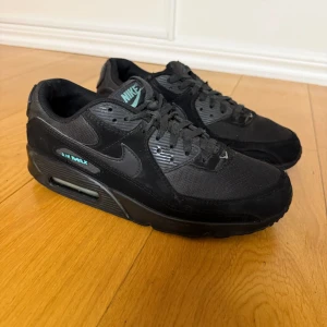 Nike Air Max 90 svarta sneakers - Svarta Nike Air Max 90 sneakers med detaljer i turkos på plösen och vid hälen. Skorna har klassisk snörning, platt sula och är tillverkade i en mix av syntet och textil. Swoosh-logga på sidan och Air Max-dämpning i sulan för extra komfort.
