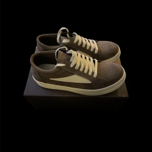 ”Rick Owens” Vans - Snygga bruna sneakers med vit sula och vit sidodetalj. Skorna har rund tå, platt sula och vita snören. Materialet är mocka med inslag av syntet, vilket ger en mjuk och stilren känsla. Perfekt för dig som gillar en clean och klassisk look.