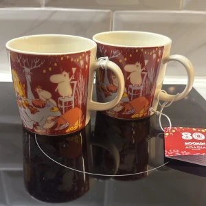 Moomin koppar -  Två Mumin-muggar från Arabia med röd dekor och motiv av Muminfamiljen. Muggarna är i nyskick och har originaletikett kvar. Perfekta för samlare eller som present. Inga defekter, säljer båda för 450kr