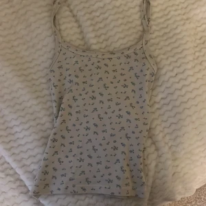 Blommig linnetopp från Brandy Melville - Säljer en söt ljusbeige linnetopp från Brandy Melville med små blå blommor över hela. 