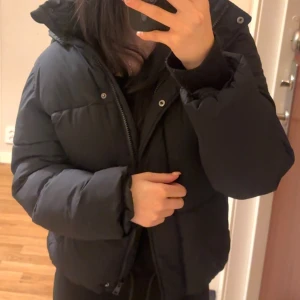 Svart pufferjacka från 157 - Svart puffer/vinter jacka från 157 med huva och dragkedja framtill , perfekt för kalla dagar. Snygg och enkel att matcha med din vardagsstil.