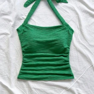 Grön ribbad halterneck linnetopp - Snygg grön halterneck topp med knyt i nacken. Toppen har en vågig mönster typ i tyget, den är lite stretch i men inte jättemycket. Jag tror de. är från vero moda. (Första bilden är u fram o andra bilden är i bak)