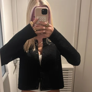 Svart fluffig kofta med knappar - Säljer en svart, mjuk och fluffig kofta med rund hals och knappar framtill. Koftan har lång ärm och en lite loose passform som ger en chill vibe. Perfekt att slänga över ett linne eller t-shirt. Materialet känns stickat och mysigt.