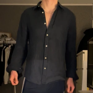 Mörkblå linneskjorta med knappar - Snygg mörkblå skjorta i linne med klassisk krage och vita knappar hela vägen. Skjortan har lång ärm och en loose passform som ger en chill vibe. Perfekt för dig som gillar stilrena plagg med enkel design och skönt material.