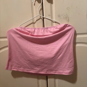 Ljusrosa bandeau tubtopp - Säljer en ljusrosa bandeau tubtopp i mjuk bomull. Toppen är axelbandslös och har en enkel, clean design med elastisk kant upptill för att sitta på plats. Perfekt för dig som gillar minimalistisk och chill stil.