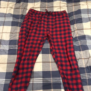 Röd-rutiga mjukisbyxor från H&M - Säljer ett par mjuka och sköna mjukisbyxor från H&M i storlek M. Byxorna har ett rött och mörkblått rutigt mönster, elastisk midja med snörning och bakficka. Perfekta för chill hemma eller häng med kompisar.
