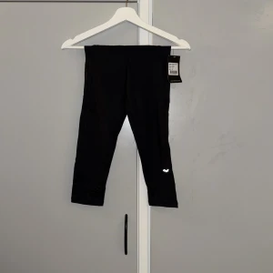 Svarta capri tights från Röhnisch XS - Svarta Janet Capri tights från Röhnisch i stretchigt syntetmaterial. De har en hög midja och reflekterande detaljer vid bensluten, perfekta för träning. Snygg och enkel design med logga på benet och bekväm passform.