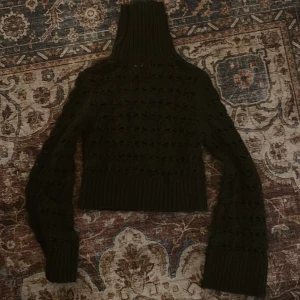 Mörkgrön stickad polotröja - Säljer en mörkgrön stickad polotröja med höga muddar och bred polokrage. Tröjan har ett genombrutet, virkat mönster och är croppad i modellen. Perfekt för lager-på-lager och en snygg detalj till din höst- eller vinterstil.