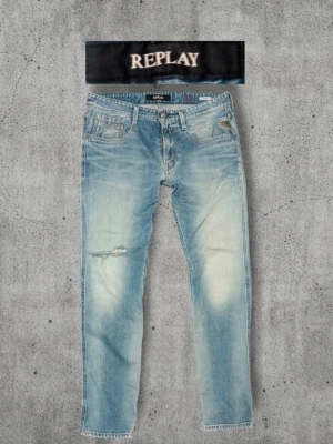 Ljusblå Replay jeans med slitningar - Säljer ett par ljusblå jeans från Replay med snygga slitningar och tvättade detaljer. Jeansen har klassisk femficksmodell, raka ben och gylf med dragkedja. Perfekta för en avslappnad och trendig stil.