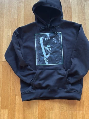 Svart The Weeknd Trilogy hoodie - Säljer en svart hoodie med stor huva och magficka. På framsidan finns ett tryck med The Weeknd och på ryggen står det 'TRILOGY' samt suddig låtlista. Perfekt för dig som gillar streetwear och musikmerch. Mjuk insida och klassisk passform. Ganska liten i storlek så för dig som har medium funkar det också.
