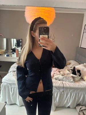 Mörkblå v-ringad kofta med knappar - Snygg mörkblå kofta med v-ringning och knäppning framtill. Långärmad och figurnära modell som passar perfekt till jeans eller kjol. Enkel och stilren design utan synligt märke.