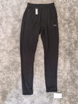  träningsbyxor  Boohoo MAN - Snygga svarta träningsbyxor från boohoo med smal passform och dragkedjor vid bensluten. Byxorna har resår i midjan, två dragkedjeförsedda fickor fram och är tillverkade i ett lätt, stretchigt material som passar perfekt för träning eller chill.
