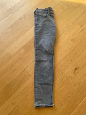 Gråa slim fit - Säljer ett par gråa skinny jeans med klassisk femficksdesign och normal midja. Jeansen har smal passform och är tillverkade i ett mjukt denimtyg med lite stretch för extra komfort. Perfekta till en avslappnad stil.