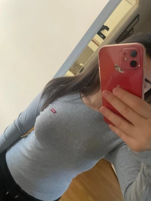 Grå långärmad topp från Levi's - Säljer en enkel och stilren grå långärmad topp från Levi's med den klassiska röda loggan på bröstet. Toppen har rund halsringning och är i ett mjukt bomullsmaterial som sitter tight och bekvämt.  Storlek Xs men passar även för storlek S