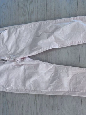 Ljusrosa chinos med raka ben - Snygga ljusrosa chinos med raka ben och klassiska fickor bak med knappstängning. Byxorna har hällor för bälte och är perfekta för en stilren look. Materialet känns mjukt och lätt, passar bra till många outfits.