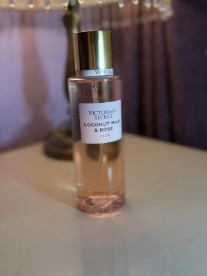 Victoria's Secret Coconut Milk & Rose - Fräsch parfymmist från Victoria's Secret med doft av kokosmjölk och ros. Flaskan är genomskinlig med ljusrosa vätska och har ett elegant guldlock. Rymmer 250 ml och ger en mjuk, blommig och tropisk känsla.