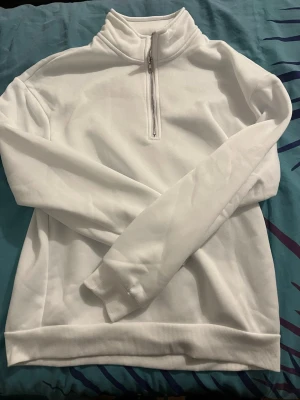 Vit halvzip hoodie med hög krage - Snygg vit hoodie med halv dragkedja och hög krage. Tröjan har långa ärmar, ribbade muddar och är tillverkad i mjukt material som känns skönt mot huden. Perfekt för en clean och stilren look.