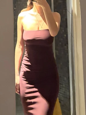 Mörklila axelbandslös klänning - Säljer en stilren, mörklila axelbandslös klänning med tight passform. Klänningen är lång och har en enkel, elegant design utan synliga detaljer. Perfekt för dig som gillar minimalistisk stil.