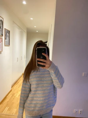 Ljusblå och grårandig stickad tröja - Mysig stickad tröja med ljusblå och grå horisontella ränder. Tröjan har rund halsringning, långa ärmar och ribbade muddar vid ärmslut och nederkant. Perfekt för kyliga dagar och enkel att matcha med jeans.