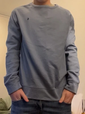 Blå crewneck från Polo Ralph Lauren - Snygg ljusblå crewneck från Polo Ralph Lauren med diskret broderad logga på bröstet. Tröjan har rund halsringning, långa ärmar och ribbade muddar. Perfekt för en avslappnad och stilren look.