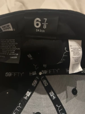 Svart La keps nästan oanvänd - Snygg svart keps från New era/La, modell 59FIFTY, med klassisk rak skärm och broderad vit logga på sidan. Kepsen är tillverkad i 100% polyester och har en stilren och modern look som passar perfekt till streetwear.