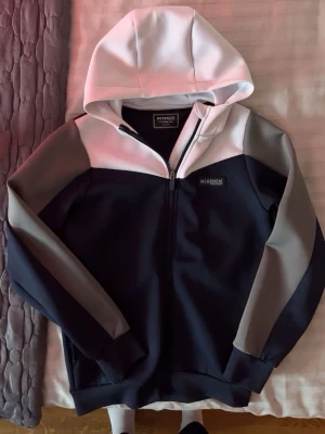 Svart och vit hoodie från McKenzie - Snygg hoodie från McKenzie i svart, vitt och grått med dragkedja framtill och huva. Hoodien har en modern colorblock-design och logga på bröstet. Perfekt för en avslappnad streetwear-look. Tillverkad i mjukt och bekvämt material.